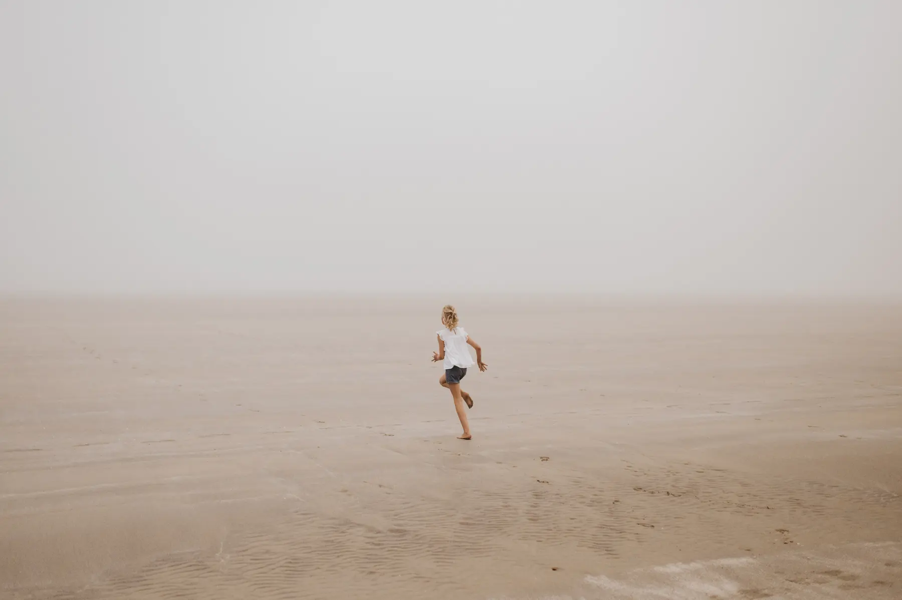 Un enfant court sur une plage prise dans la brume.