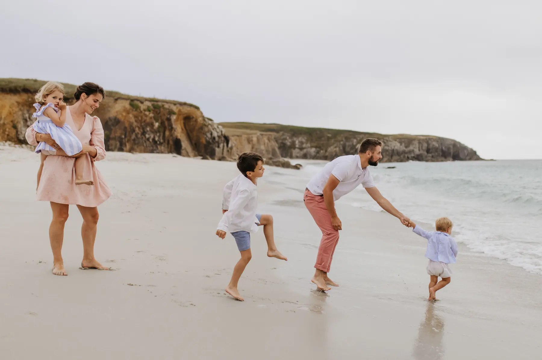 Une famille court sur la plage au pied de la falaise.