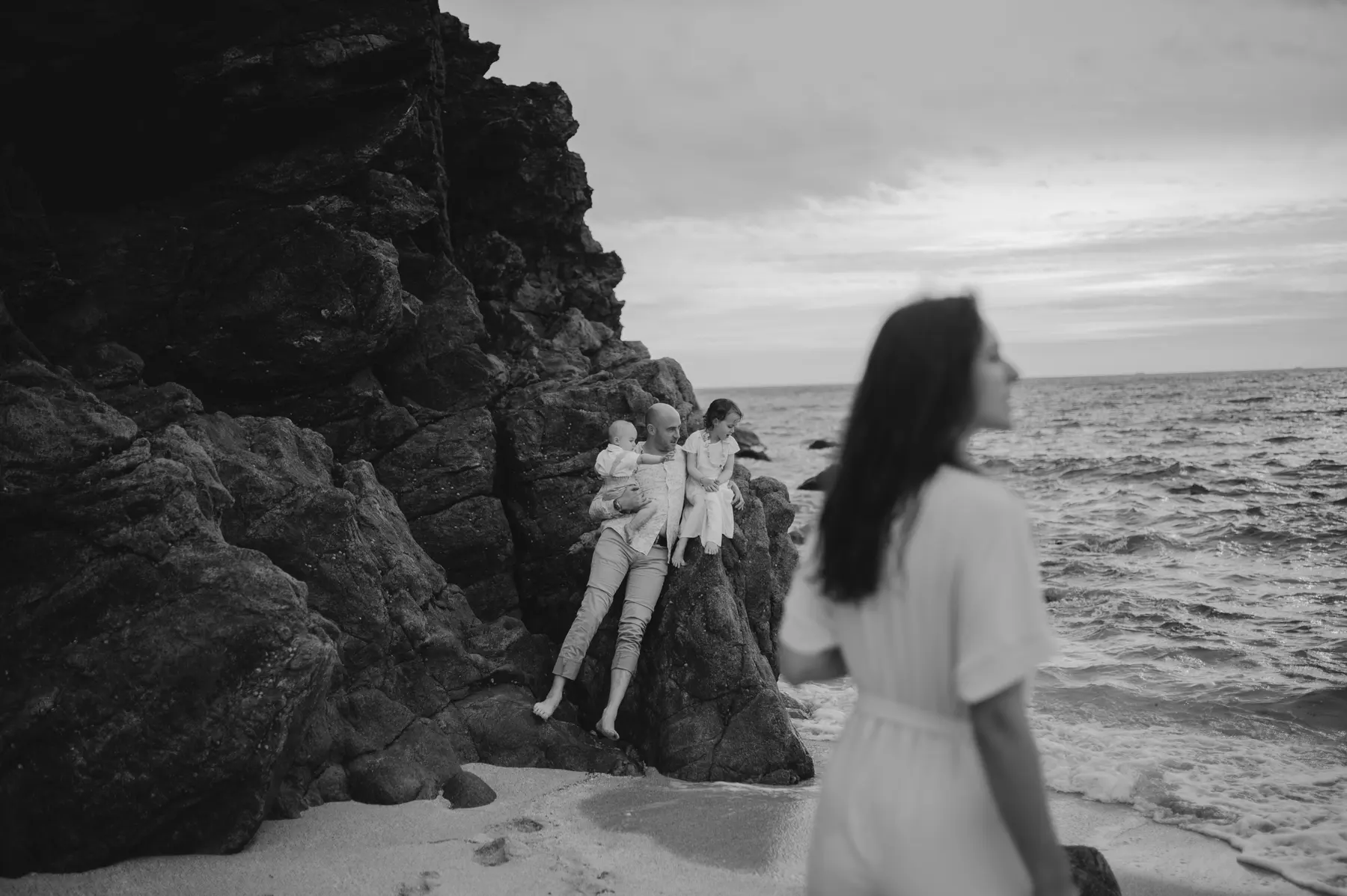 Une femme et ses enfants sur les rochers, en noir et blanc.