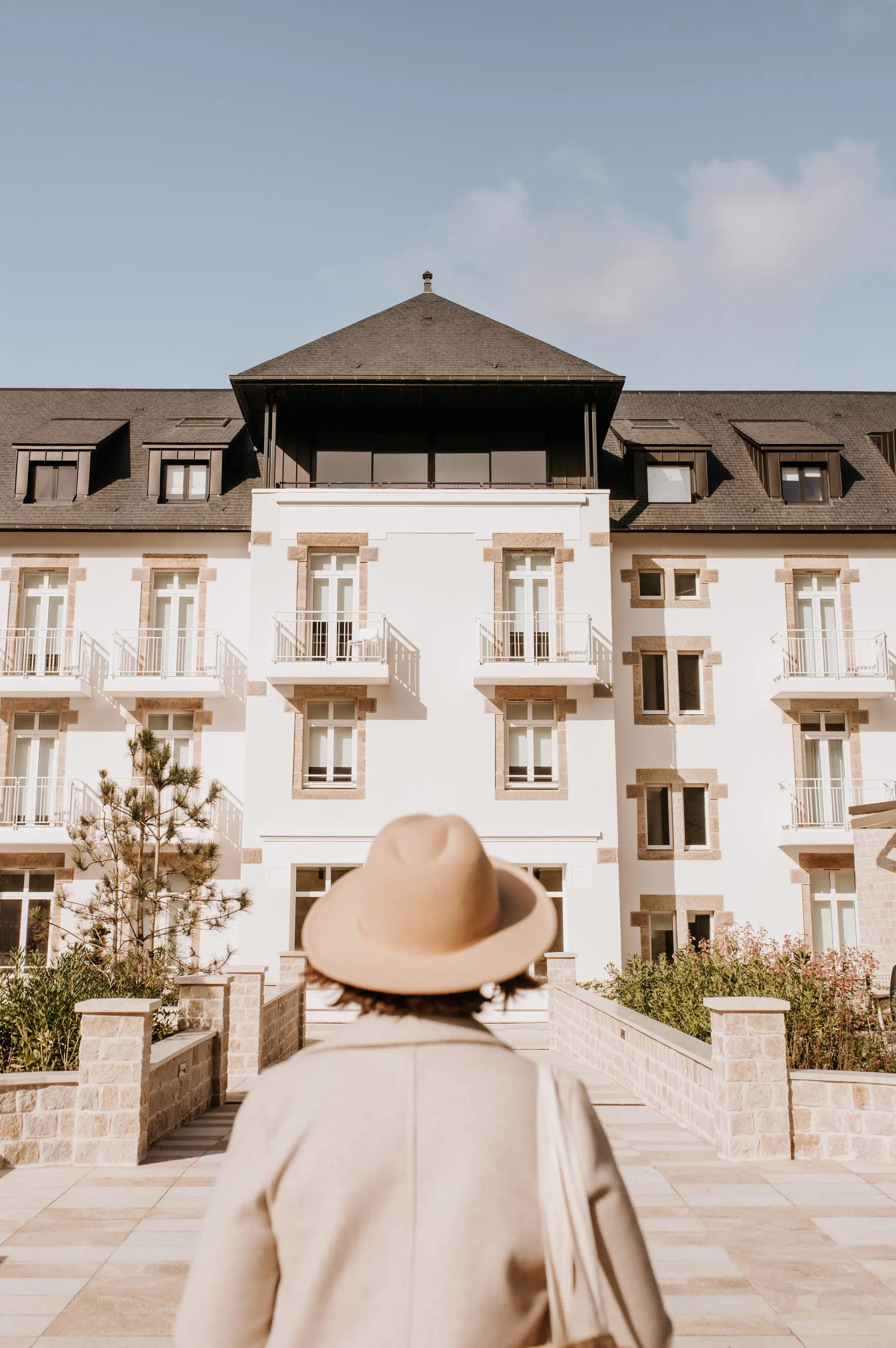 Une femme au chapeau devant la façade d’un hôtel.