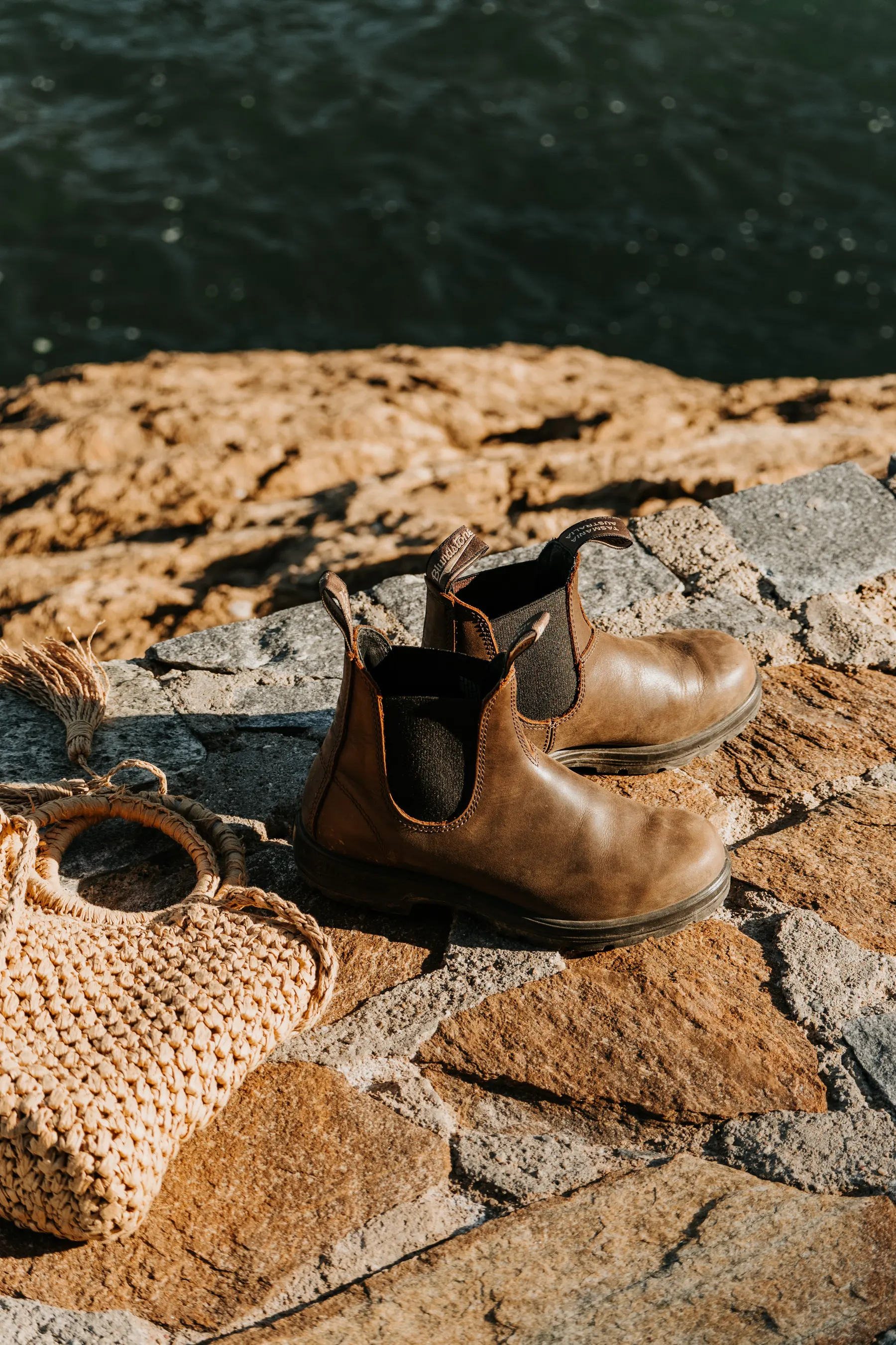 Des bottines et un sac d’osier posés sur des rochers.