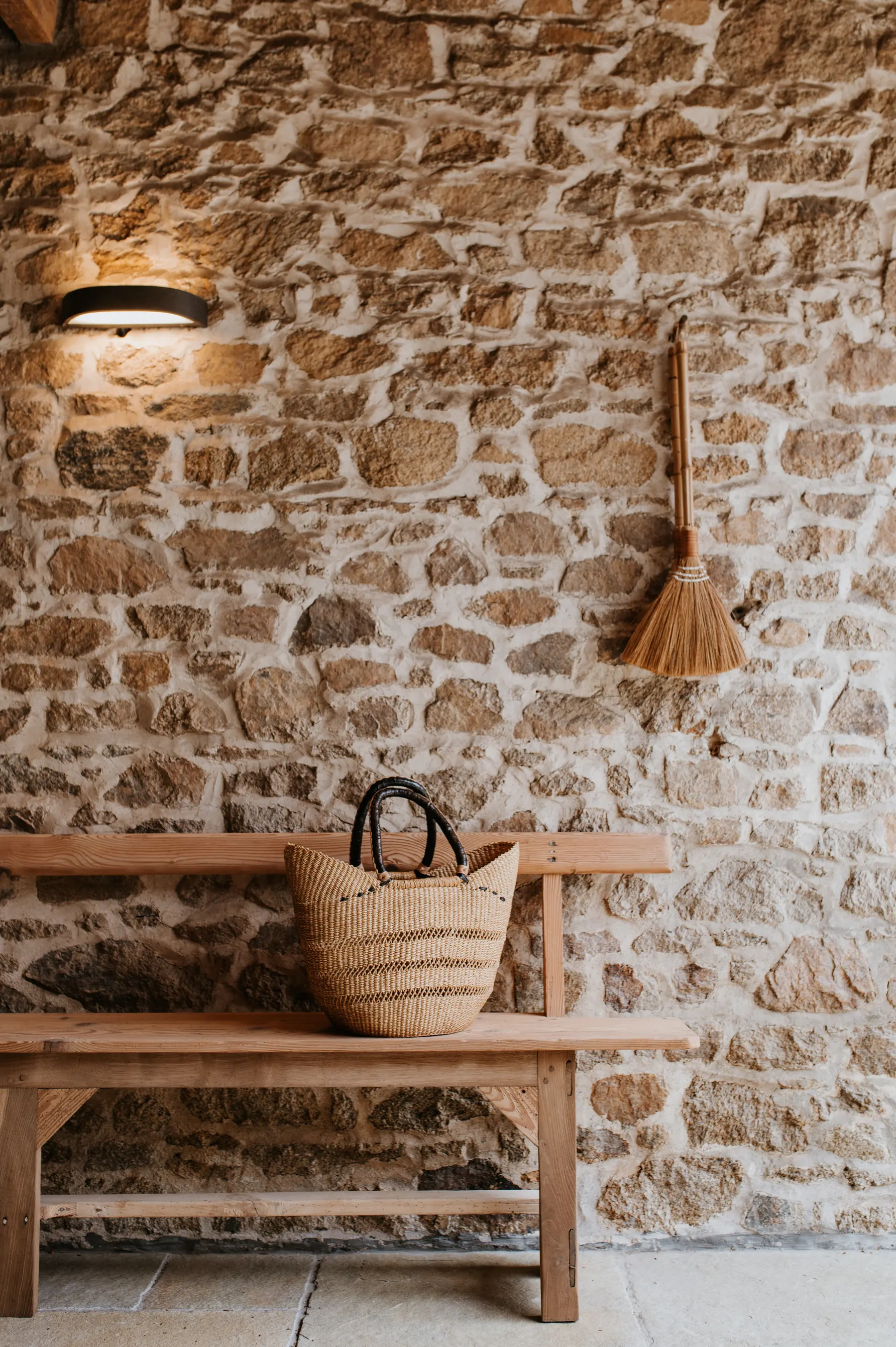 L'entrée en pierre d'une maison d'hôtes, un banc de bois et un panier d'osier posés contre le mur.