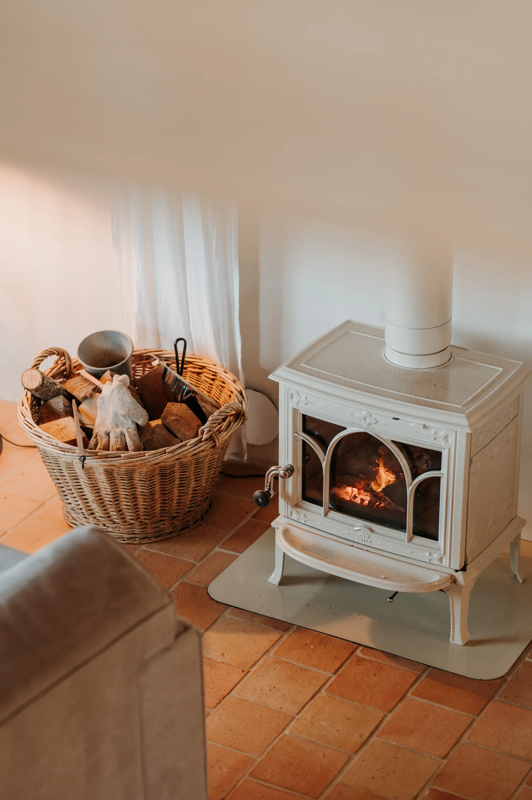 Un poêle à bois blanc et son panier de bûches, dans un intérieur clair.