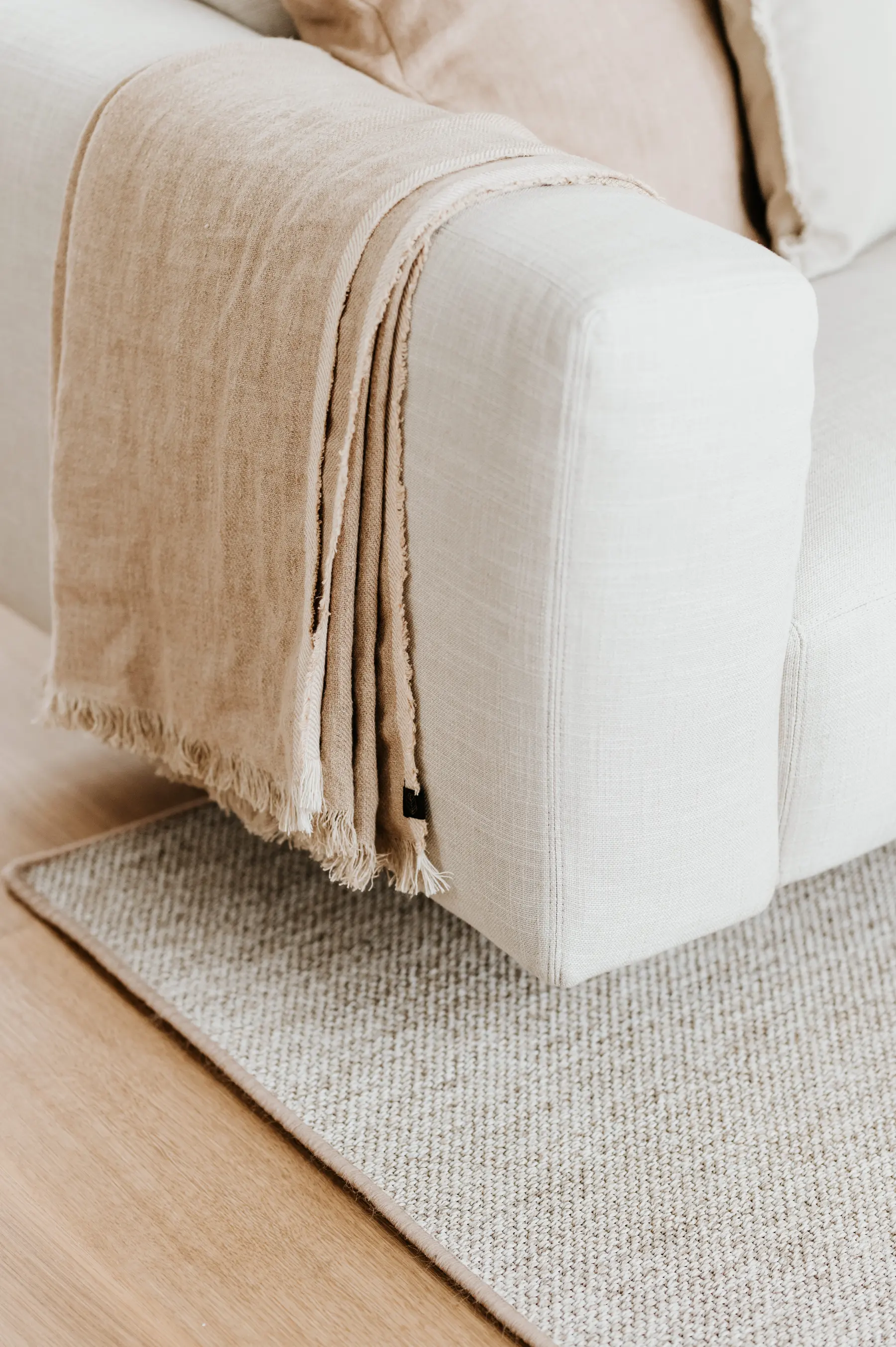 Un canapé beige recouvert d’un plaid de lin froissé.