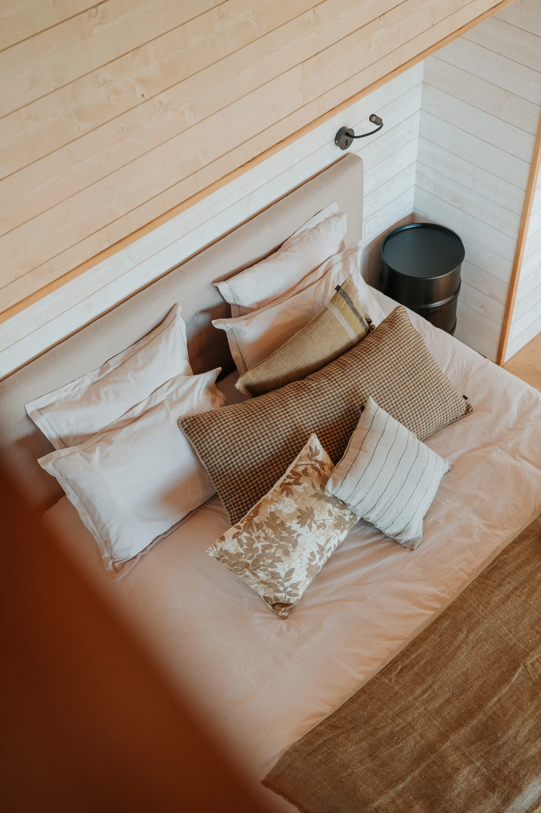 Un lit vu de haut dans une chambre lambrissée de bois clair.