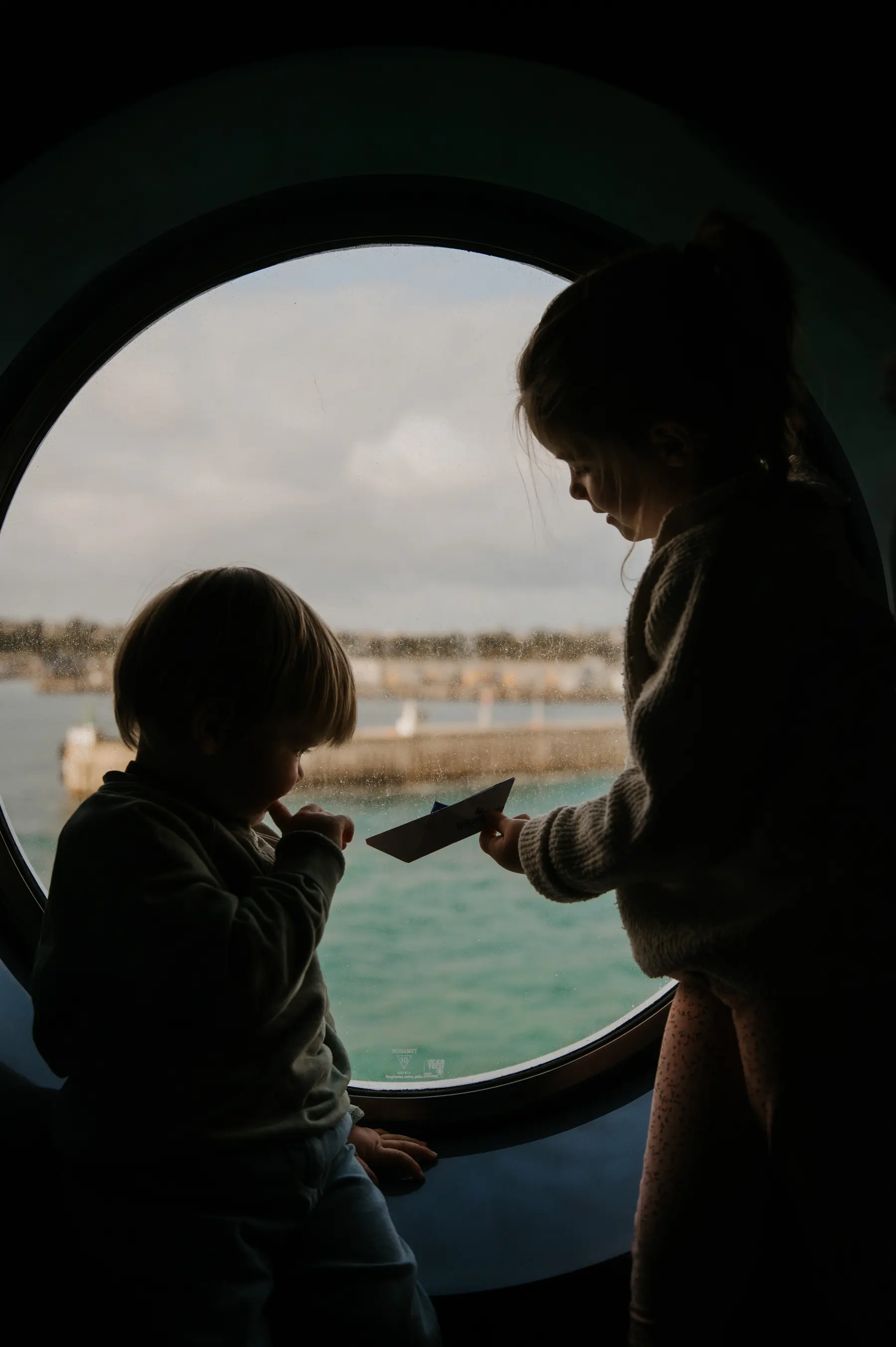 Silhouettes d’une femme et d’un enfant devant un hublot.